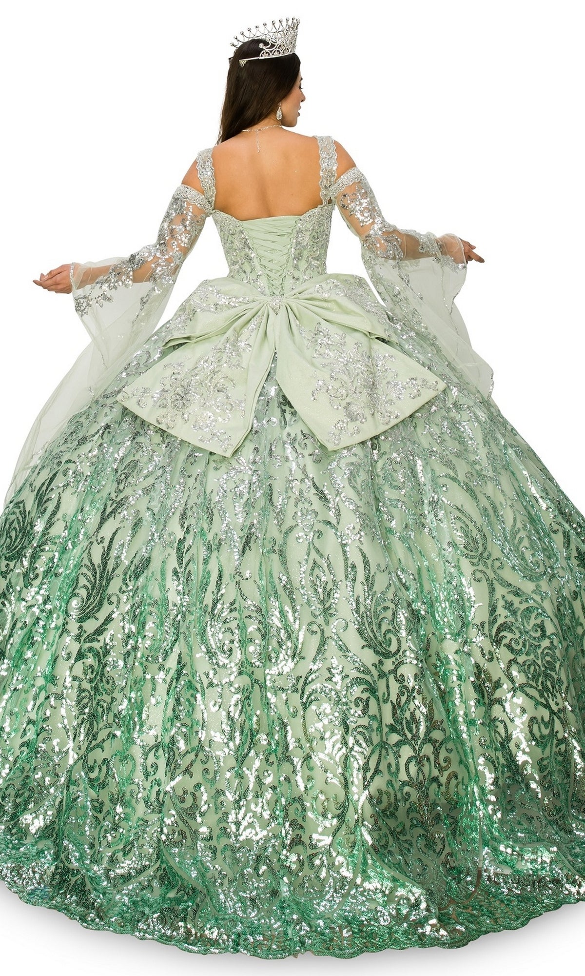 A woman, shown from the back with arms slightly raised, wears the Quinceanera Ball Gown 8080J—a large green ombre ball gown adorned with silver sequins and a crown.